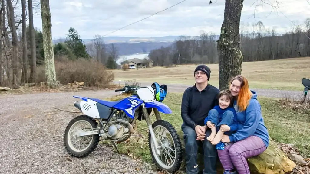 Adam, Judy, and their son with a dirt bike on the farm, the lake in the distance